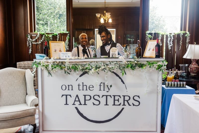 The On The Fly Tapsters branded portable bar set up indoors with greenery along the front
