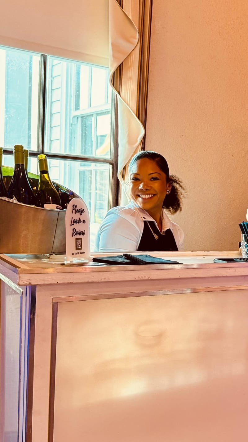 Smiling bartender behind a bar with wine bottles chilling beside her