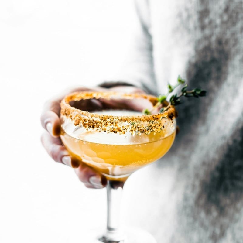 A finished cocktail in a coupe glass with a garnished rim, held in one hand